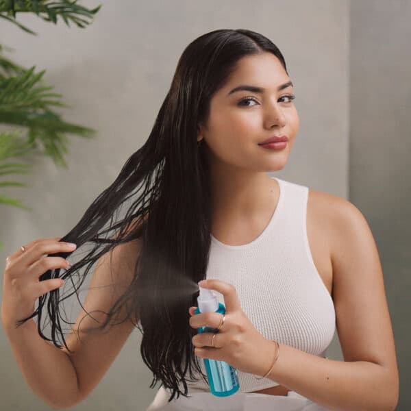 Mujer aplicando Frizz Shield Spray de Moroccanoil en su cabello mojado.