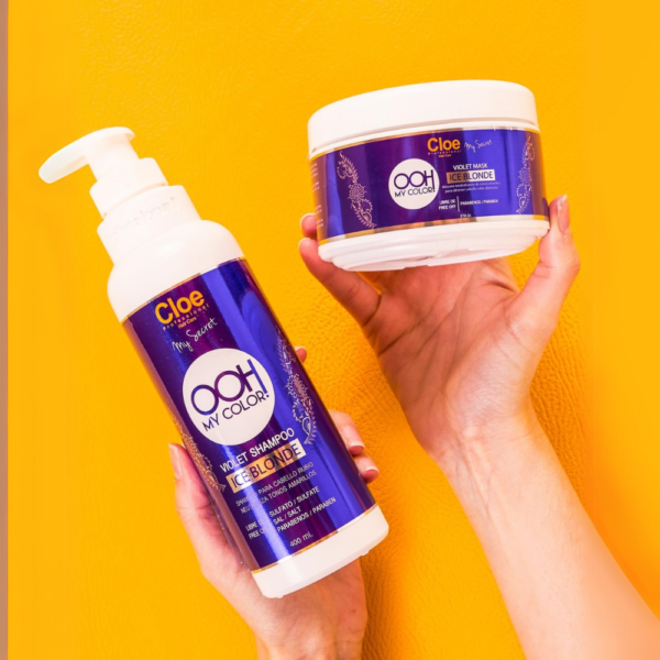 Persona sosteniendo botella de shampoo y envase de mascarilla Cloe OOH My Color Violet Mask Ice Blonde sobre fondo amarillo vibrante.