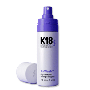 Botella de shampoo en seco K18 AirWash de 118 ml con tapa blanca colocada al lado. La botella es blanca con detalles morados y letras negras, mostrada sobre fondo blanco.