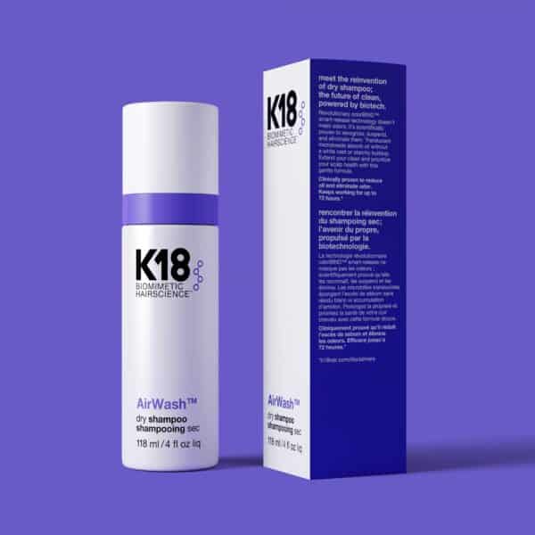 Botella de shampoo en seco K18 AirWash de 118 ml junto a su caja, ambos sobre fondo morado. La botella es blanca con tapa morada y letras negras, y la caja muestra texto informativo en inglés y francés.