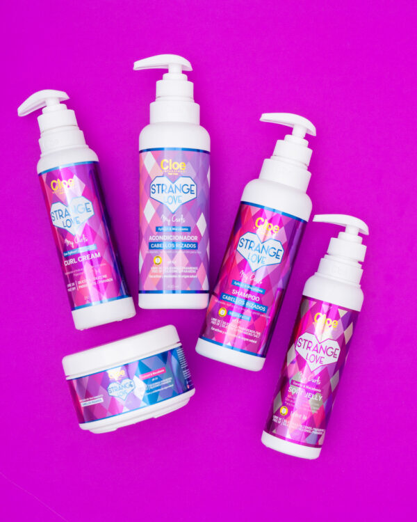 Cinco productos de la línea Strange Love My Curls para cabellos rizados, dispuestos sobre fondo fucsia, resaltando shampoo, acondicionador, curl cream, soft jelly y máscara.
