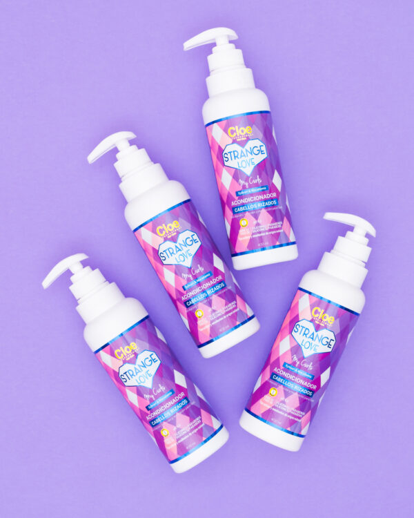 Cuatro botellas de Acondicionador Strange Love My Curls para cabellos rizados, dispuestas sobre fondo morado, destacando su fórmula sin siliconas ni parabenos.