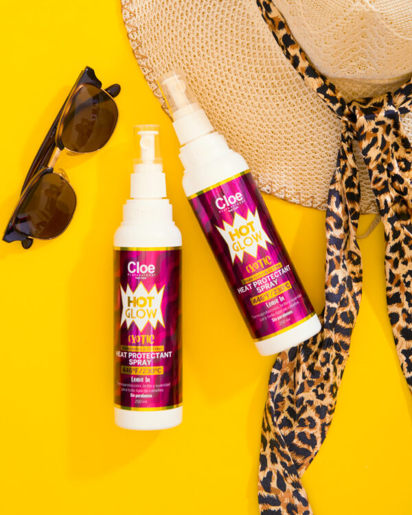 Dos botellas de Cloe Hot Glow Exotic Heat Protectant Spray sobre fondo amarillo, acompañadas de gafas de sol y sombrero con cinta animal print.