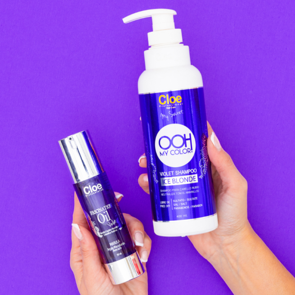 Manos sosteniendo botella de shampoo y frasco de óleo Cloe OOH My Color sobre fondo morado. Ambos productos tienen etiquetas moradas con detalles plateados.