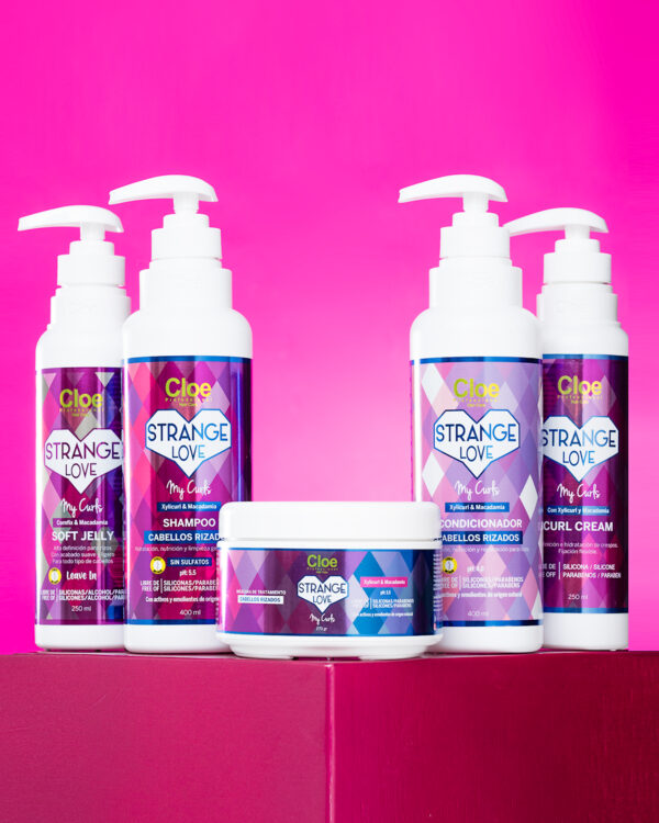roductos completos de la línea Strange Love My Curls para cabellos rizados sobre fondo rosado, incluyendo shampoo, acondicionador, curl cream, soft jelly y máscara.