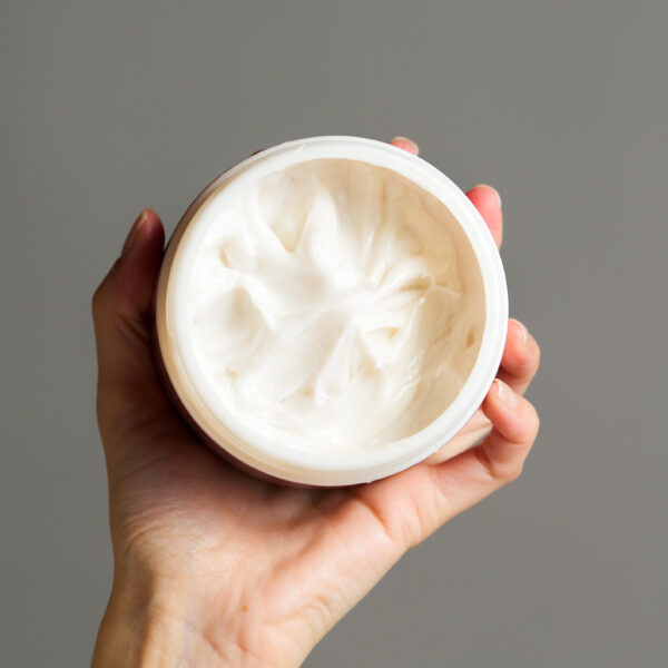 Vista superior de envase abierto de mascarilla Rouvé Bond Recovery sostenido por una mano, mostrando la textura blanca cremosa del producto.