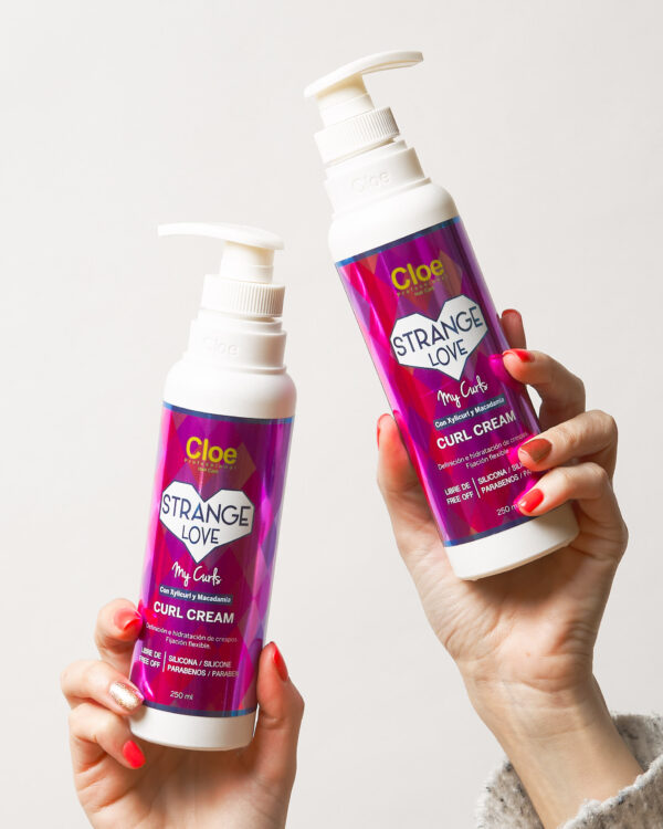 os botellas de Curl Cream Strange Love My Curls de 250 ml sostenidas por manos, mostrando el diseño del envase para definición e hidratación de rizos.