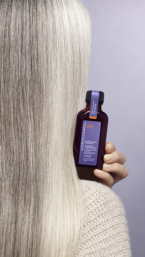 Tratamiento Moroccanoil Purple en mano con fondo de cabello gris claro